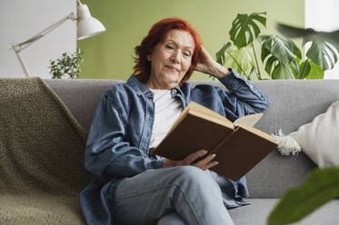 Entspannte ältere Frau liest ein Buch auf dem Sofa zu Hause - ALKF01054