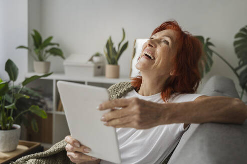 Ältere Frau mit Tablet-PC lachend im heimischen Wohnzimmer - ALKF01061