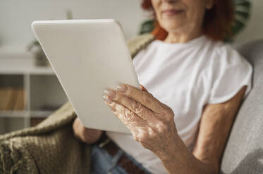 Frau im Ruhestand mit digitalem Tablet, die zu Hause auf dem Sofa sitzt - ALKF01063