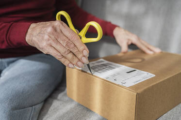 Hand of senior woman opening cardboard box on sofa - ALKF01067