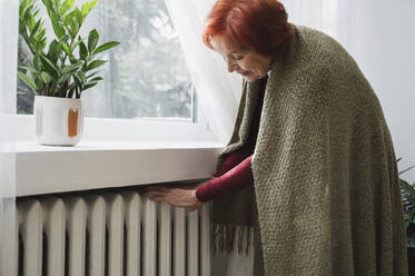 Ältere Frau prüft die Temperatur des Heizkörpers zu Hause - ALKF01071