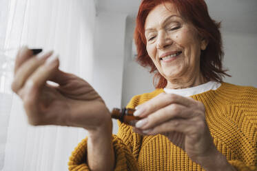 Smiling senior woman applying essential oil on wrist at home - ALKF01081