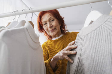 Senior woman with tops hanging on rack in closet - ALKF01095