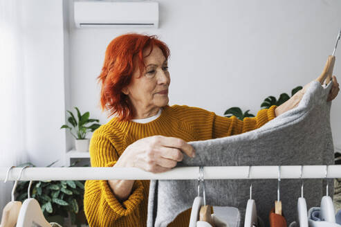 Ältere Frau im Ruhestand wählt einen Pullover aus dem Kleiderständer zu Hause aus - ALKF01096