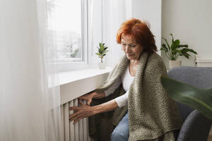 Ältere rothaarige Frau prüft die Temperatur des Heizkörpers zu Hause - ALKF01099