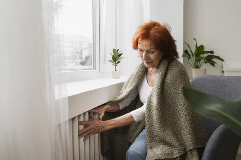 Ältere rothaarige Frau prüft die Temperatur des Heizkörpers zu Hause - ALKF01099