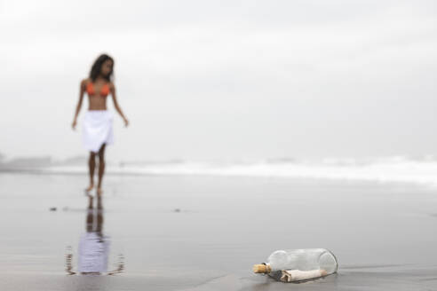 Message in glass bottle with woman on wet sand at beach - EAF00141