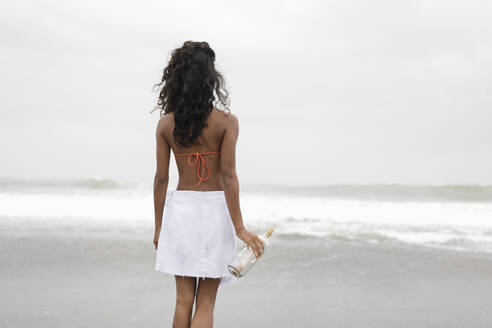 Woman holding message in bottle and looking at sea - EAF00142