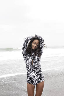 Woman wearing rash guard and standing with arms raised at beach - EAF00145