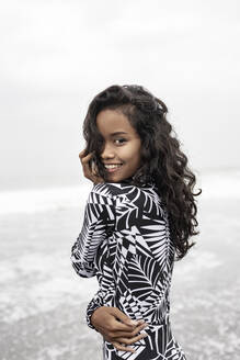 Smiling young woman in patterned rash guard at beach - EAF00146