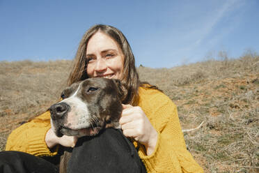 Glückliche Frau mit Hund auf einem Hügel sitzend - KVBF00066