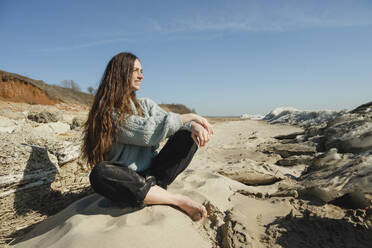 Lächelnde Frau sitzt auf einem Felsen an einem sonnigen Tag - KVBF00068