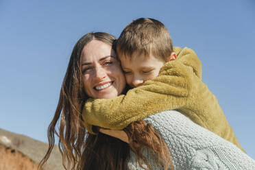 Son with arm around mother under clear sky - KVBF00074