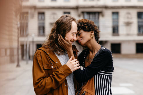 An image capturing a moment of affection between a young couple as they embrace on a quiet street in the city, portraying love, connection, and urban life. - JLPSF31460