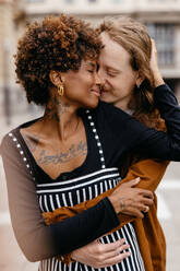 An intimate moment captured between a young couple in love, embracing each other on an urban sidewalk, showcasing genuine affection and a close bond. - JLPSF31464