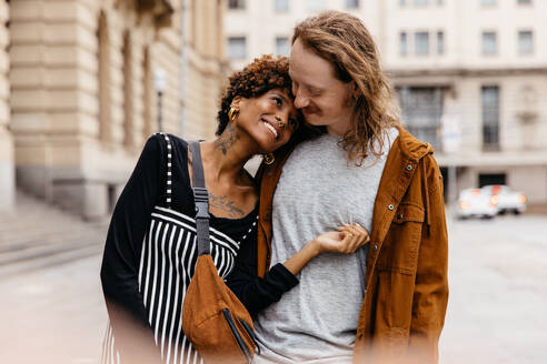 A young couple is captured in a loving embrace on an urban street, conveying warmth, romance, and connection amid the cityscape. - JLPSF31468