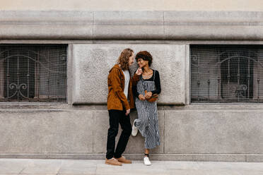 A candid capture of a young couple enjoying a romantic moment together while standing on an urban street. Their casual style and affectionate pose convey a feeling of love and companionship in the hustle of city life. - JLPSF31473