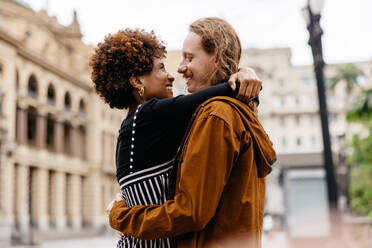 A young couple in love shares an embrace on a city street, presenting a sense of romance, connection and urban life. This image captures a tender moment in a busy world. - JLPSF31481