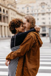 This image captures a tender moment between a young couple as they lovingly embrace on a city street, showcasing their affection and connection amidst an urban backdrop. - JLPSF31482