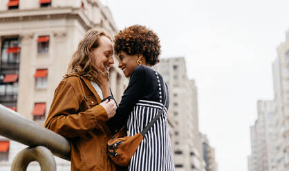 A young and affectionate couple shares a loving embrace on a bustling city street, capturing a candid moment of romance amidst the urban landscape. - JLPSF31488