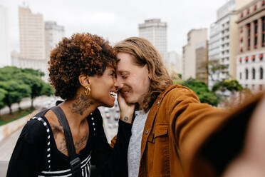 A young and affectionate couple enjoying each other's company in an urban setting. Their laughter and closeness evoke feelings of love and togetherness amidst the busy city life. - JLPSF31490