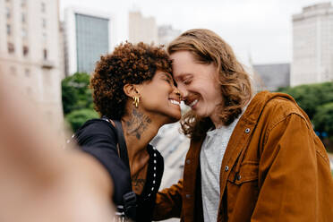 A loving young couple sharing a tender moment on a city street. They are close and smiling, exuding a sense of happiness, intimacy, and urban romance. Perfect for themes of love, diversity, and relationships in an urban setting. - JLPSF31492