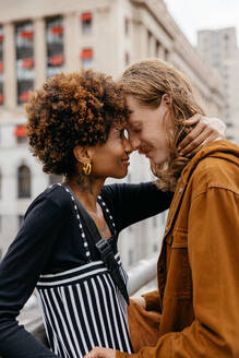 A young, loving couple enjoys a tender moment together while embracing on a bustling city street, radiating affection and connection in an urban setting. - JLPSF31493