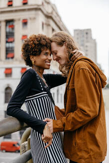 A tender moment between a young couple, lovingly wrapped in an embrace on a city street, sharing a connection amidst the urban backdrop. - JLPSF31494