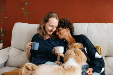 A heartwarming scene of a couple enjoying a cozy moment on the sofa at home, sipping coffee with their adorable dog by their side. Captures the essence of domestic bliss and companionship. - JLPSF31506