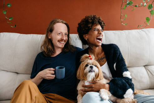 A comfortable and loving atmosphere as a couple laughing together and sharing quality time with their pet dog. Cuddling and enjoying a warm drink, showcasing a serene and homely vibe. - JLPSF31510