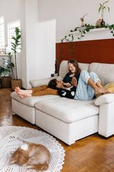 A loving couple shares a tender moment lounging comfortably on a sofa in a well-decorated living room, with a dog resting peacefully on the floor. - JLPSF31514