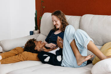 A candid shot capturing a sweet moment between a smiling couple lying down on a cozy sofa, conveying warmth, affection, and domestic happiness. - JLPSF31515