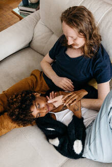 A heartwarming image of a couple in casual attire, lounging intimately together on a comfortable couch, exuding love and closeness in a homey setting. - JLPSF31516