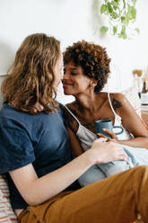 A candid shot of a loving couple sharing a close and personal moment. The image captures their smiles and eye contact, exuding the warmth and affection between them as they relax together in a comfortable home setting, creating an atmosphere of intimacy and togetherness. - JLPSF31523