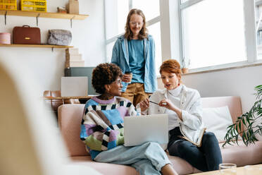 Three diverse colleagues engage in a project discussion in a bright freelance co-working space. They appear focused and comfortable, embodying a professional yet casual work environment. - JLPSF31529