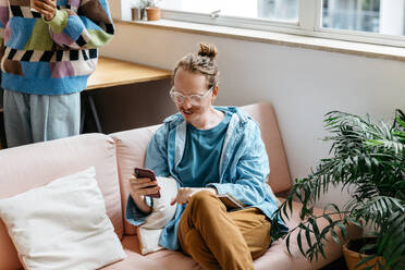 A freelance work setting capturing two colleagues collaborating in a co-working space. The relaxed environment features a woman on a couch using a smartphone, embodying the flexible and contemporary work culture. - JLPSF31531