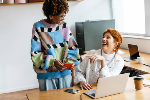 Two professionals engage in a collaborative work session in a bright, contemporary freelance office environment. They are immersed in productivity and teamwork, utilizing laptops and smartphones to facilitate their innovative tasks. - JLPSF31548