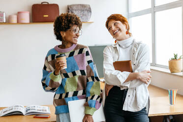 Two professional freelancers working together in a bright co-working environment. They convey a sense of teamwork and productivity in a casual office setting, with coffee and laptops as common work tools. - JLPSF31555