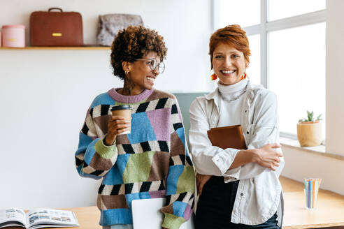 Two creative professionals enjoy a casual meeting in a well-lit co-working space. With notebooks in hand and coffee to fuel their day, they embody the modern freelance lifestyle. - JLPSF31556