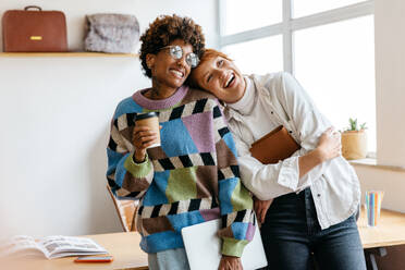 Two happy colleagues taking a break, laughing together in a freelance office setting. They evoke a sense of companionship and positivity in a casual co-working environment. - JLPSF31557