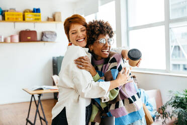 A warm, friendly office environment as colleagues share a mutual embrace in a bright co-working space. The image portrays themes of teamwork, support, and professional camaraderie in a freelance office setting. - JLPSF31560