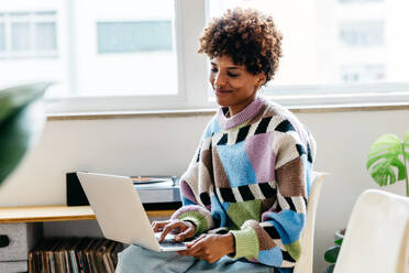 A happy female freelancer focused on her work at a laptop in a vibrant, well-lit co-working space. The image depicts modern freelance work and collaboration in a modern office setting. - JLPSF31580