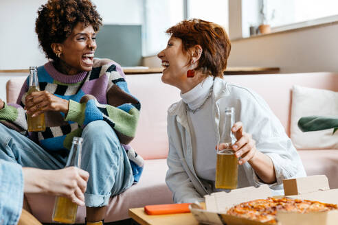 Freelance professionals taking a break in a co-working environment, enjoying a casual meeting with drinks and pizza. A moment of relaxation and camaraderie in the workspace. - JLPSF31589