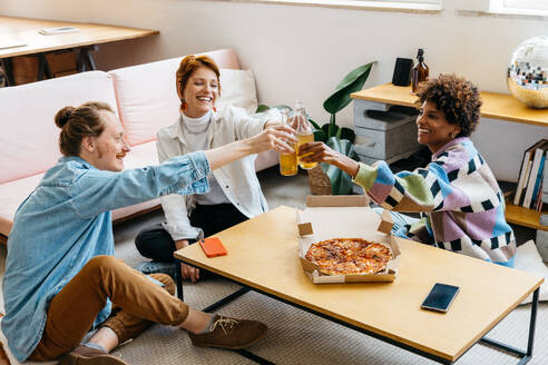 Freelance professionals share a casual moment, toasting drinks over a delicious pizza in a bright and contemporary co-working space. A perfect blend of work and relaxation, capturing teamwork and community. - JLPSF31592