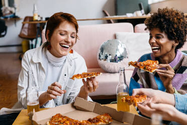 Two happy colleagues share a moment of joy as they take a break from work to enjoy pizza together in a freelance co-working space, promoting a relaxed and friendly office atmosphere. - JLPSF31610