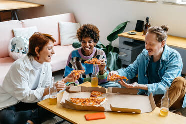 A diverse group of colleagues enjoy a casual lunch break with pizza and drinks, bonding over food in a modern co-working environment, fostering a sense of community and teamwork. - JLPSF31654