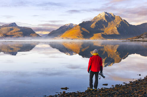 A photographer observes mountains and rorbuer in a Fjord during sunset, Leknes, Vestvagoy, Nordland, Lofoten Islands, Norway, Scandinavia, Europe - RHPLF32509