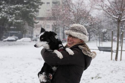 Blonde Frau, winterlich gekleidet mit Pelzmütze und Schal, spielt mit ihrem Hund, Mailand, Italien - ISF26288