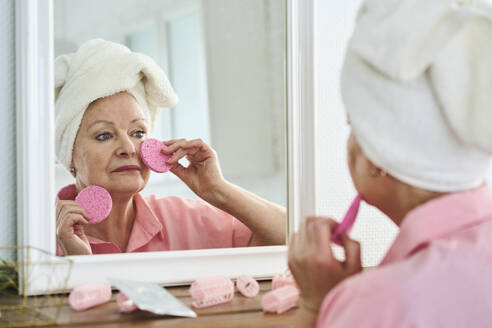 Woman wearing towel and taking care of skin looking in mirror at home - DMBF00030