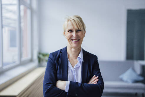 Smiling businesswoman standing with arms crossed in office - JOSEF23883